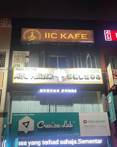 The building at night, with the lit IIC KAFE sign at the top.